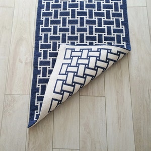 May include: A blue and white geometric patterned rug with a woven design. The rug is folded in half, revealing the back side.