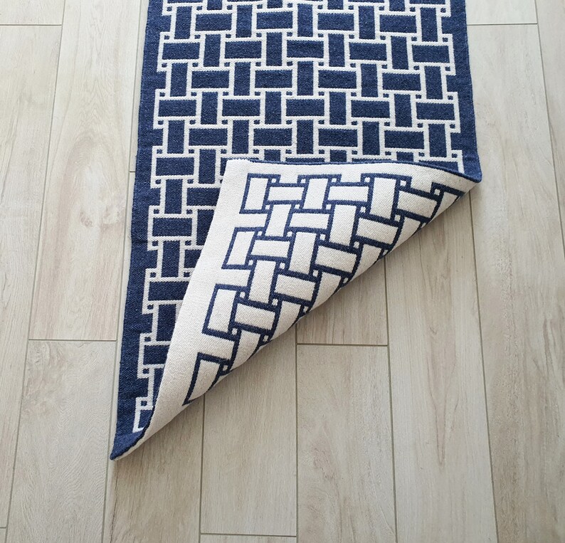 May include: A blue and white geometric patterned rug with a woven design. The rug is folded in half, revealing the back side.
