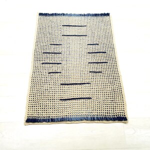 May include: A beige woven rug with a fringe border and dark blue stripes.