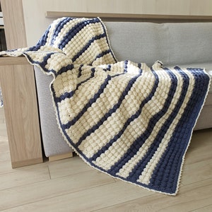 May include: A white and blue striped crocheted throw blanket with a textured bobble stitch. The blanket is draped over a couch.