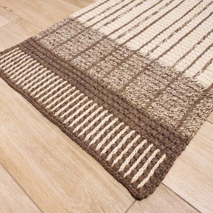 May include: A brown and cream striped rug with a textured woven design. The rug has a thick border with a repeating pattern of vertical stripes.
