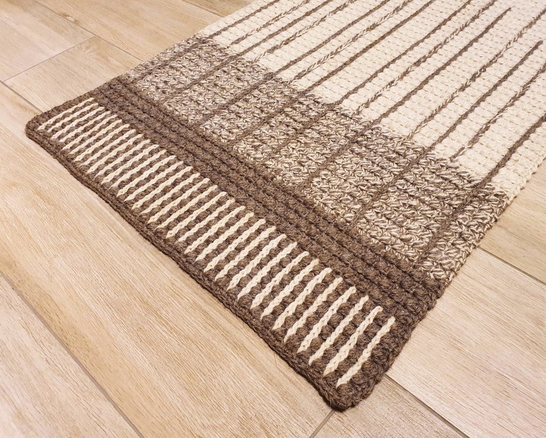 May include: A brown and cream striped rug with a textured woven design. The rug has a thick border with a repeating pattern of vertical stripes.