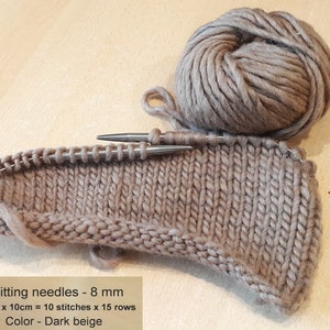 May include: A close-up of a dark beige knitted fabric with knitting needles. The fabric is 10 cm by 10 cm and has 10 stitches by 15 rows. The knitting needles are 8 mm. The text "Knitting needles - 8 mm 10cm x 10cm = 10 stitches x 15 rows Color - Dark beige" is visible in the image.