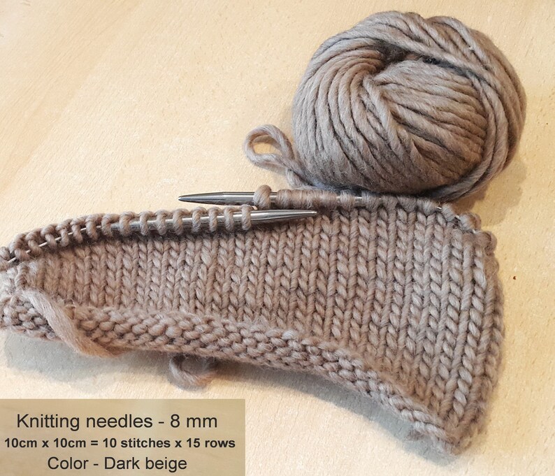 May include: A close-up of a dark beige knitted fabric with knitting needles. The fabric is 10 cm by 10 cm and has 10 stitches by 15 rows. The knitting needles are 8 mm. The text "Knitting needles - 8 mm 10cm x 10cm = 10 stitches x 15 rows Color - Dark beige" is visible in the image.