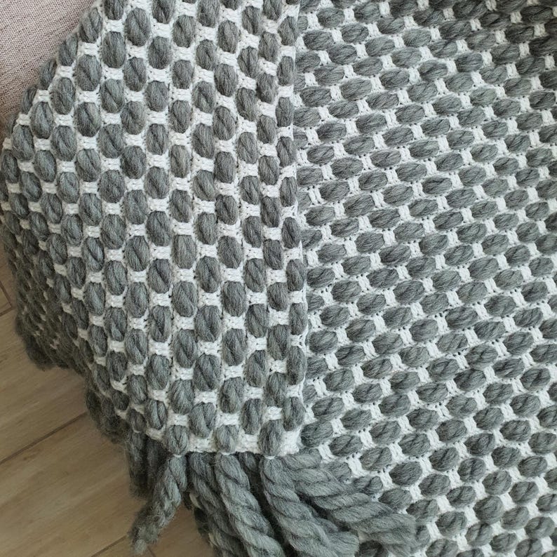 Close-up of crochet wool blanket showing thick yarn, dense stitches and textured surface in gray color