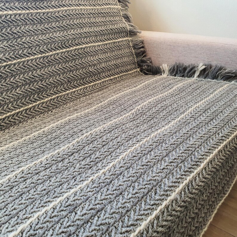A gray and white striped throw blanket with a fringe border. The blanket is made of a soft, textured fabric and is perfect for adding a touch of warmth and style to any room.