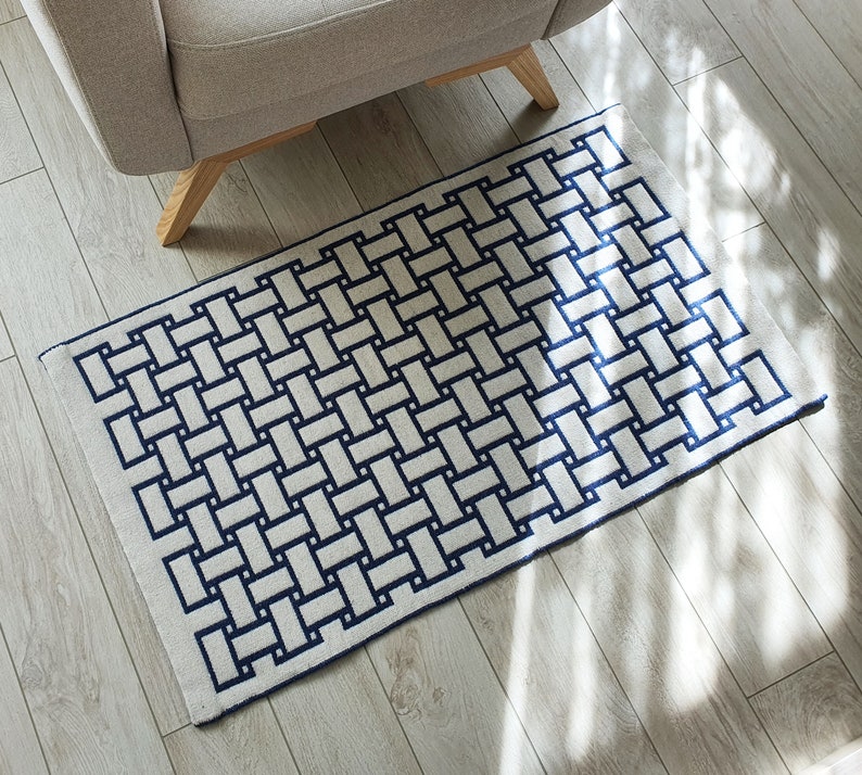 May include: A white and blue woven rug with a geometric pattern. The rug has a rectangular shape and is made of a soft, durable material.