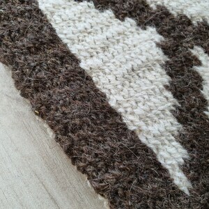 May include: Close-up of a woven rug with brown and white stripes. The rug is made of natural fibers and has a textured surface.