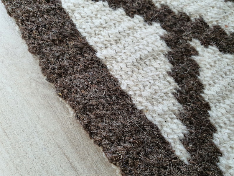 May include: Close-up of a woven rug with brown and white stripes. The rug is made of natural fibers and has a textured surface.