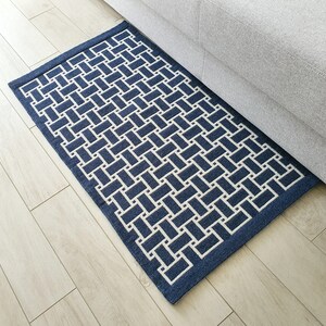 May include: A blue and white geometric patterned rug with a woven texture. The rug is placed on a light wood floor.