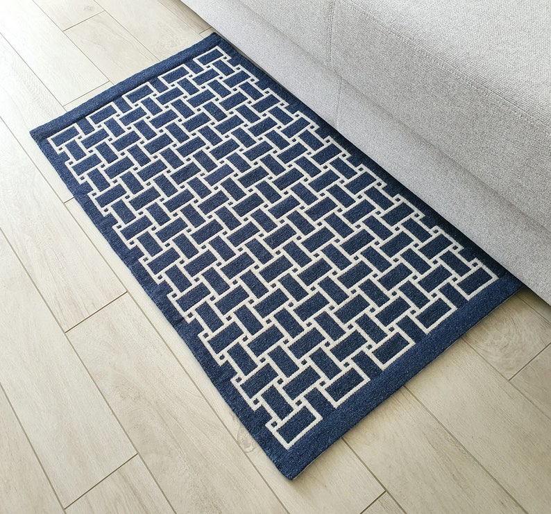 May include: A blue and white geometric patterned rug with a woven texture. The rug is placed on a light wood floor.
