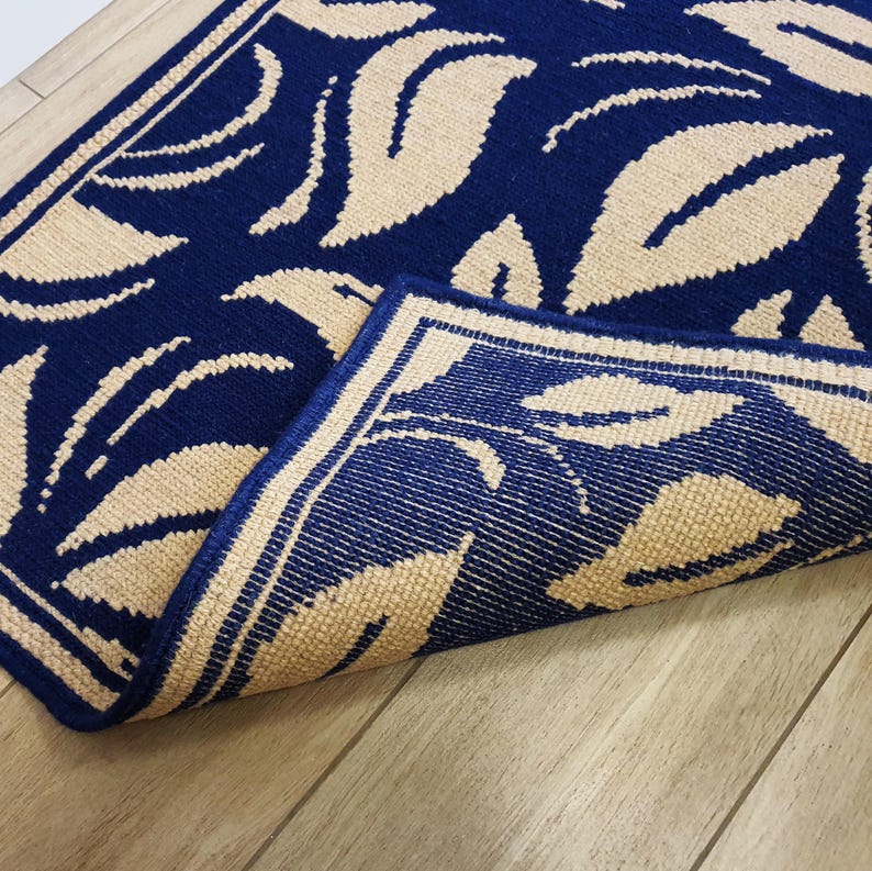 A blue and beige patterned doormat with a floral design. The doormat is folded in half, showing the back side.