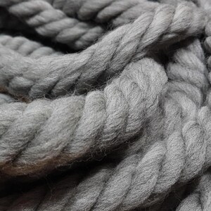 May include: Close-up of a thick, gray rope. The rope is tightly twisted, with visible texture and a soft, woolly appearance. The color is a solid, muted gray, suggesting a natural fiber product.