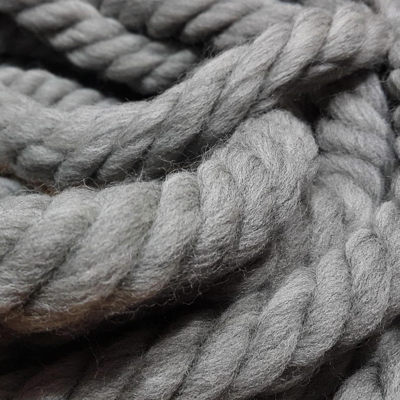 May include: Close-up of a thick, gray rope. The rope is tightly twisted, with visible texture and a soft, woolly appearance. The color is a solid, muted gray, suggesting a natural fiber product.
