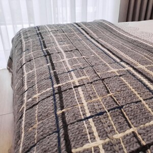 A gray knitted throw blanket with a white and black plaid pattern. The blanket is made of thick yarn and has a soft, cozy texture.