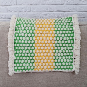 May include: A square decorative pillow with a green and white dotted pattern and a yellow stripe down the center. The pillow has a white fringe border. The pillow is approximately 16 inches square.