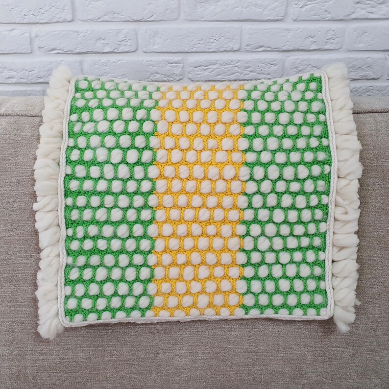May include: A square decorative pillow with a green and white dotted pattern and a yellow stripe down the center. The pillow has a white fringe border. The pillow is approximately 16 inches square.
