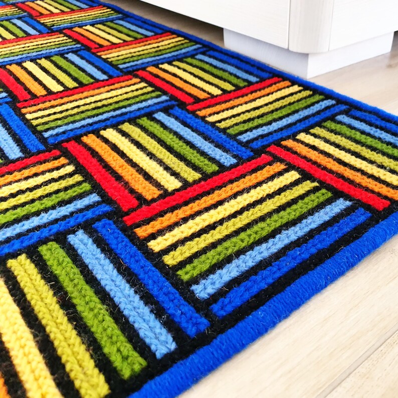 A vibrant handmade wool carpet featuring rows of alternating vertical and horizontal stripes.