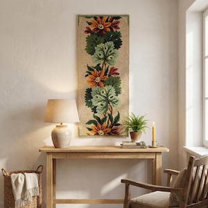Handmade wool embroidery panel featuring floral pattern with green leaves, decorative wall hanging on the light wall. over a small table.