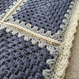 May include: Close-up of a crocheted blanket with a blue and gray pattern and a beige border.