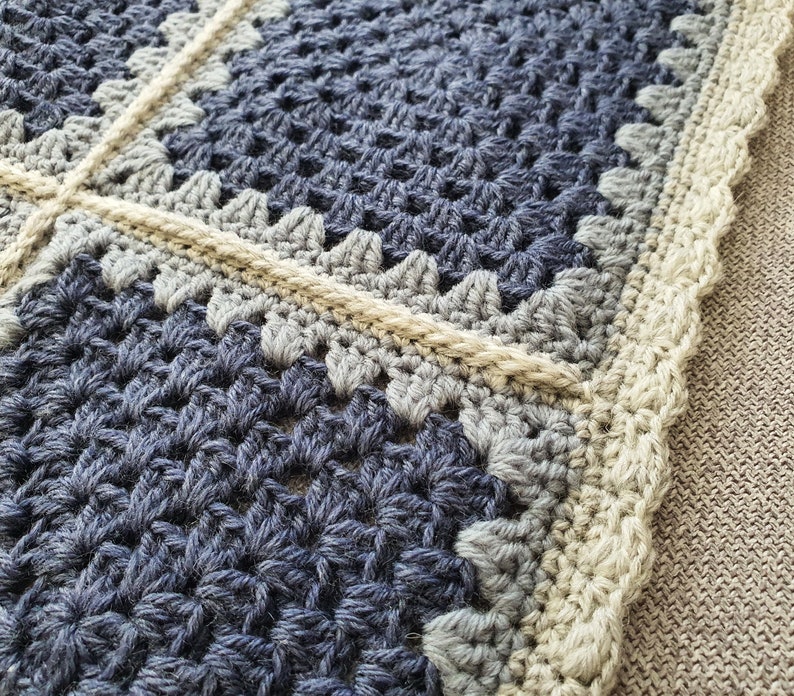 May include: Close-up of a crocheted blanket with a blue and gray pattern and a beige border.