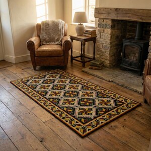 handmade embroidered wool rug in burgundy and yellow colors, It is placed on the dark wooden floor next to a fireplace in a living room.
