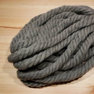 One skein of the chunky wool yarn in gray on a wooden background. Yarn is twisted fiber that is durable and washable.