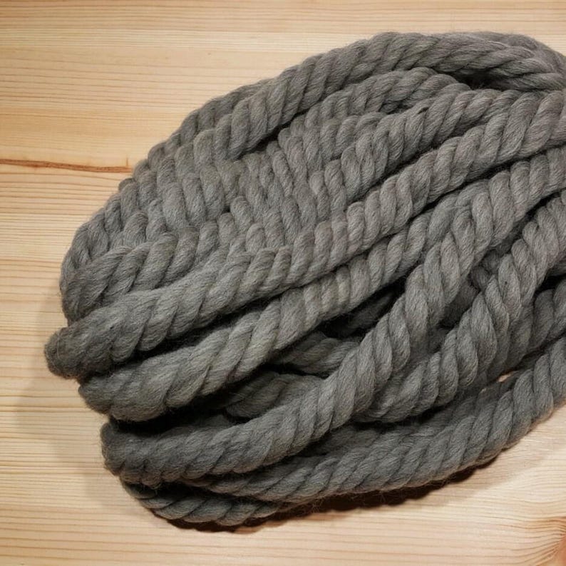 One skein of the chunky wool yarn in gray on a wooden background. Yarn is twisted fiber that is durable and washable.