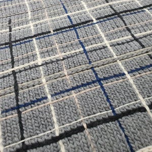 Close-up of a gray knitted fabric with a plaid pattern. The fabric is woven with white, black, and blue threads.