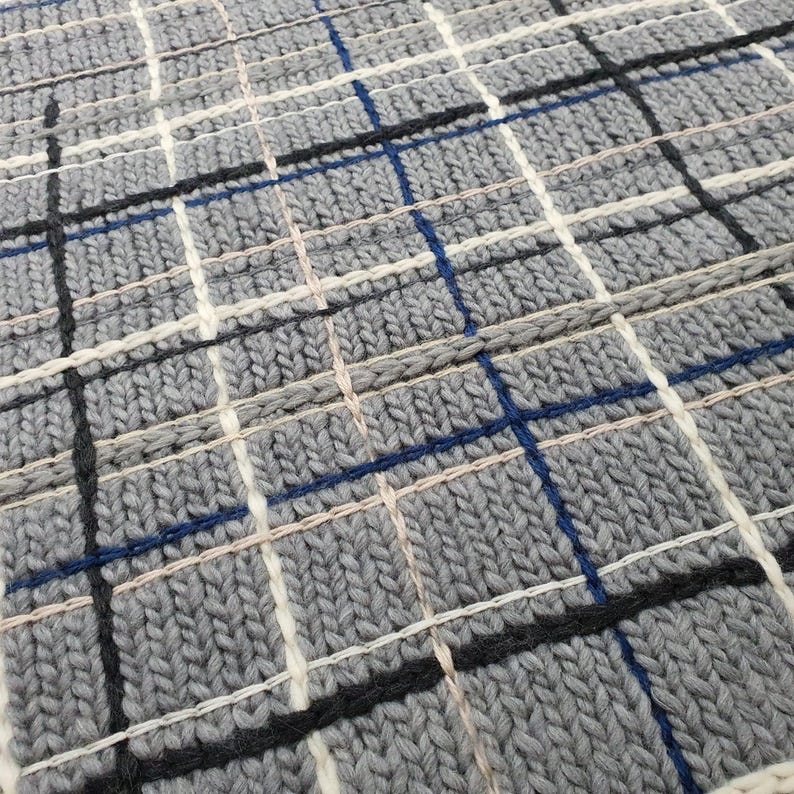 Close-up of a gray knitted fabric with a plaid pattern. The fabric is woven with white, black, and blue threads.