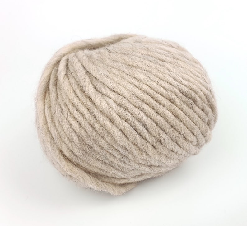 May include: A ball of beige yarn, made from wool, is shown against a white background.
