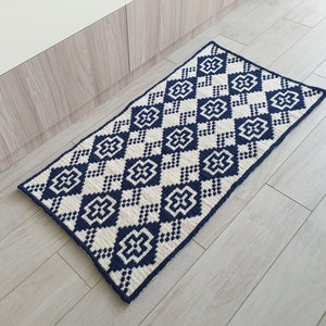 May include: A navy blue and white geometric patterned rug with a diamond design. The rug is made of a soft, woven material and has a fringed edge.