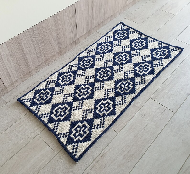 May include: A navy blue and white geometric patterned rug with a diamond design. The rug is made of a soft, woven material and has a fringed edge.