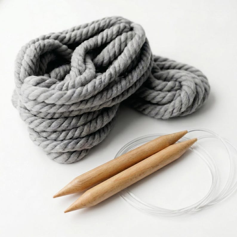 One ball of the chunky wool yarn in gray next to a knitting needles circular. Yarn is twisted fiber that is durable and washable.