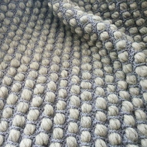Peut inclure: Gros plan sur un tissu gris textur&eacute; avec un motif r&eacute;p&eacute;titif de bosses arrondies en relief. Le tissu a un aspect tiss&eacute; avec des bosses gris clair et un fond gris plus fonc&eacute;.