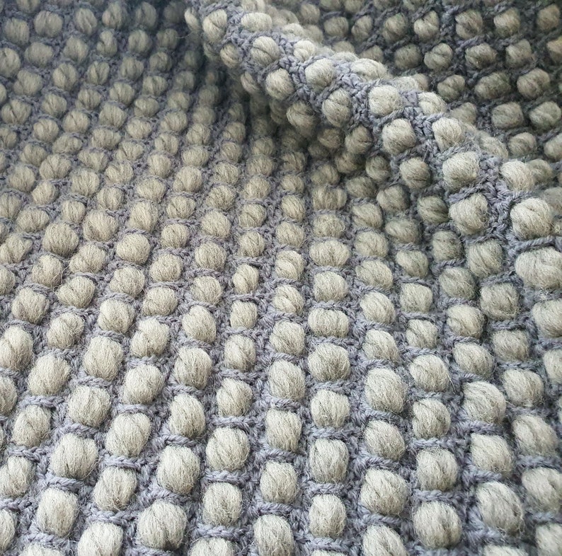 Peut inclure: Gros plan sur un tissu gris textur&eacute; avec un motif r&eacute;p&eacute;titif de bosses arrondies en relief. Le tissu a un aspect tiss&eacute; avec des bosses gris clair et un fond gris plus fonc&eacute;.