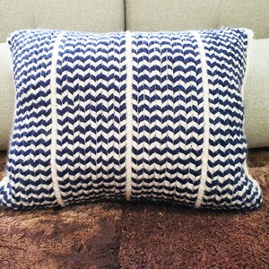 May include: A blue and white striped throw pillow with a chevron pattern. The pillow is made of a soft, textured fabric.