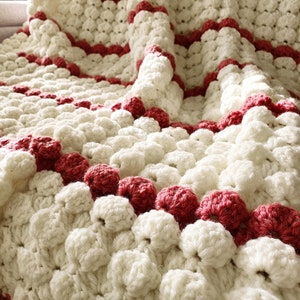 Close-up a white and red crocheted blanket with a textured, puffy design. The blanket has a repeating pattern of white circles with red stripes.