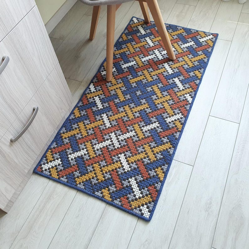 A blue, orange, white, and yellow geometric patterned rug with a woven texture. The rug is on a light wood floor.