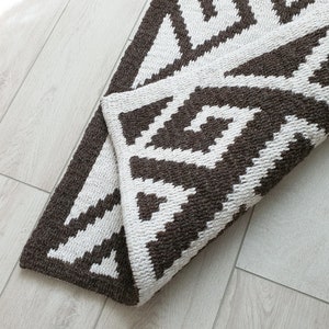 May include: A brown and white geometric patterned rug with a woven texture. The rug is folded in half and the pattern is visible on both sides.