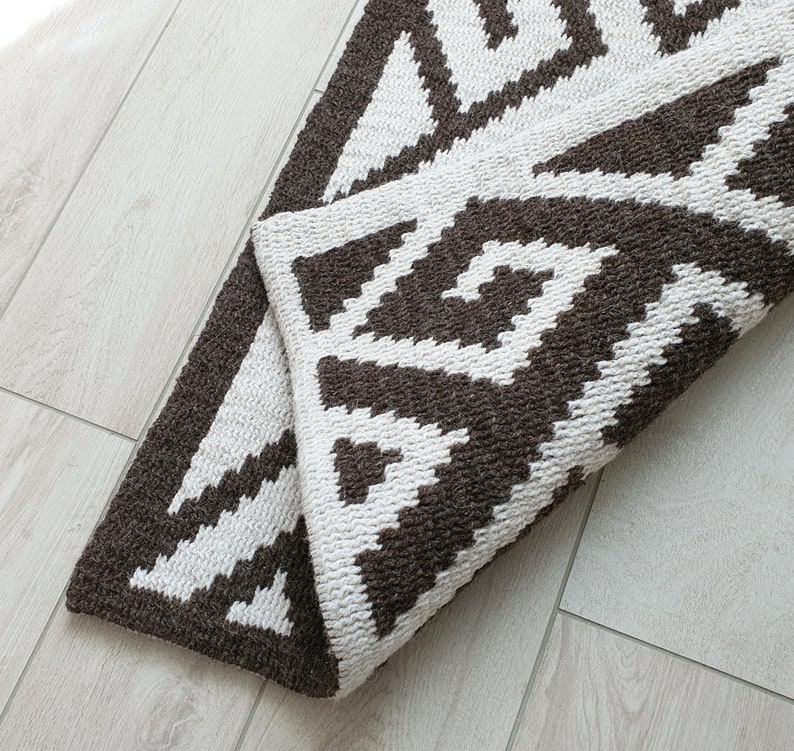 May include: A brown and white geometric patterned rug with a woven texture. The rug is folded in half and the pattern is visible on both sides.