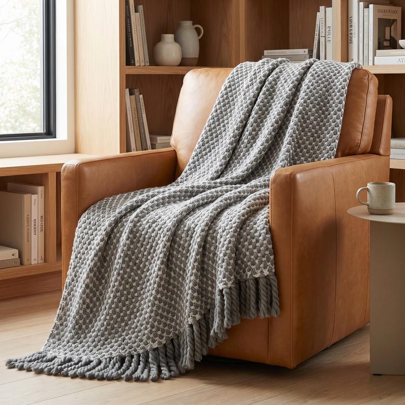 Neutral gray wool throw blanket with soft folds and heavy texture on leather chair