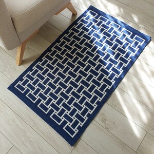 May include: A blue and white geometric patterned rug with a woven design. The rug has a border of a darker blue color.