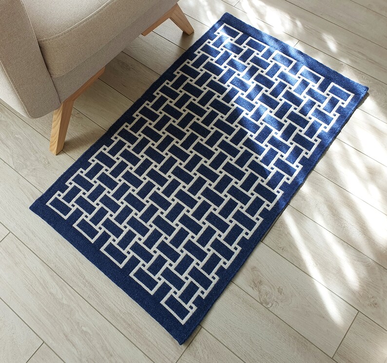 May include: A blue and white geometric patterned rug with a woven design. The rug has a border of a darker blue color.