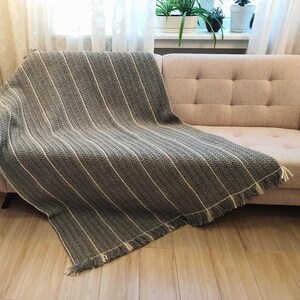 Handmade wool throw in gray color draped over a sofa, showing textured crochet pattern.