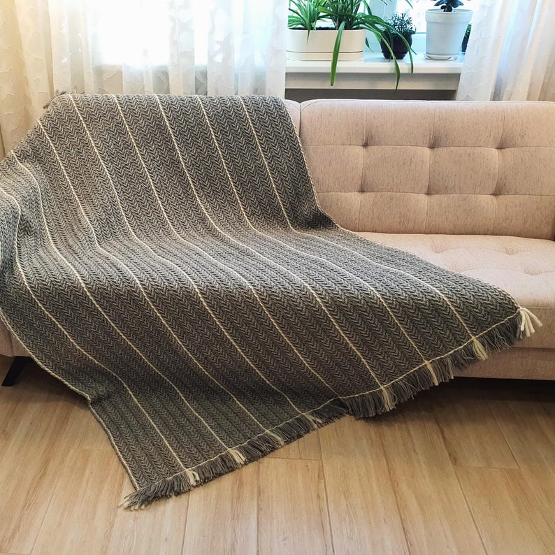 Handmade wool throw in gray color draped over a sofa, showing textured crochet pattern.