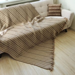 Handmade wool throw in beige color draped over a sofa, showing textured crochet pattern