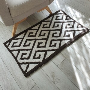 May include: A brown and white geometric patterned rug with a diamond design. The rug is on a light wood floor.