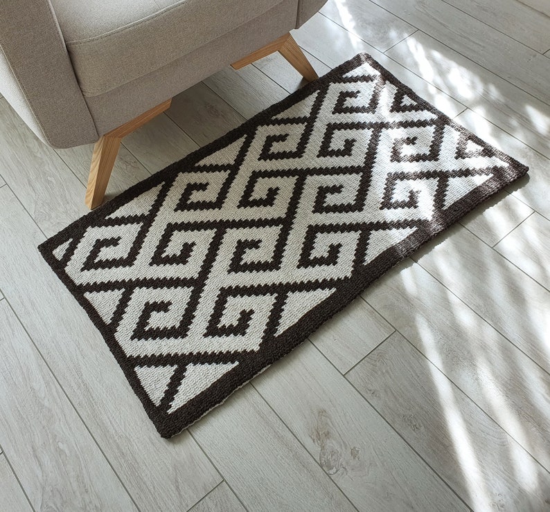 May include: A brown and white geometric patterned rug with a diamond design. The rug is on a light wood floor.