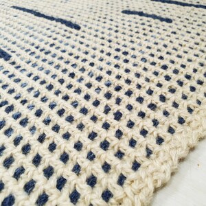 May include: Close-up of a woven rug with a natural beige background and blue stripes. The rug is made of a natural fiber and has a textured surface.